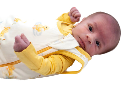Newborn baby wearing a yellow and white bamboo sleep sack on a white background