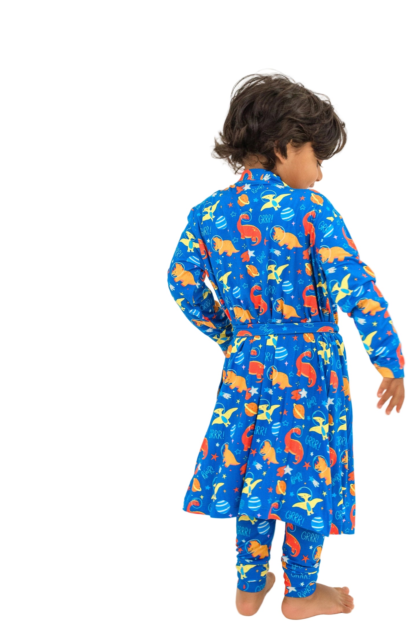A toddler standing with their back to the camera, wearing a blue long-sleeve pajama set with a colorful fish pattern, photographed against a seamless white studio background.