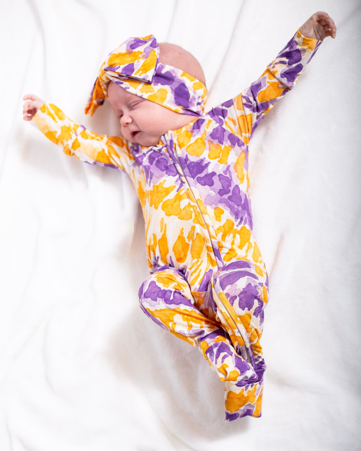 Baby in a purple and yellow patterned outfit on a white background