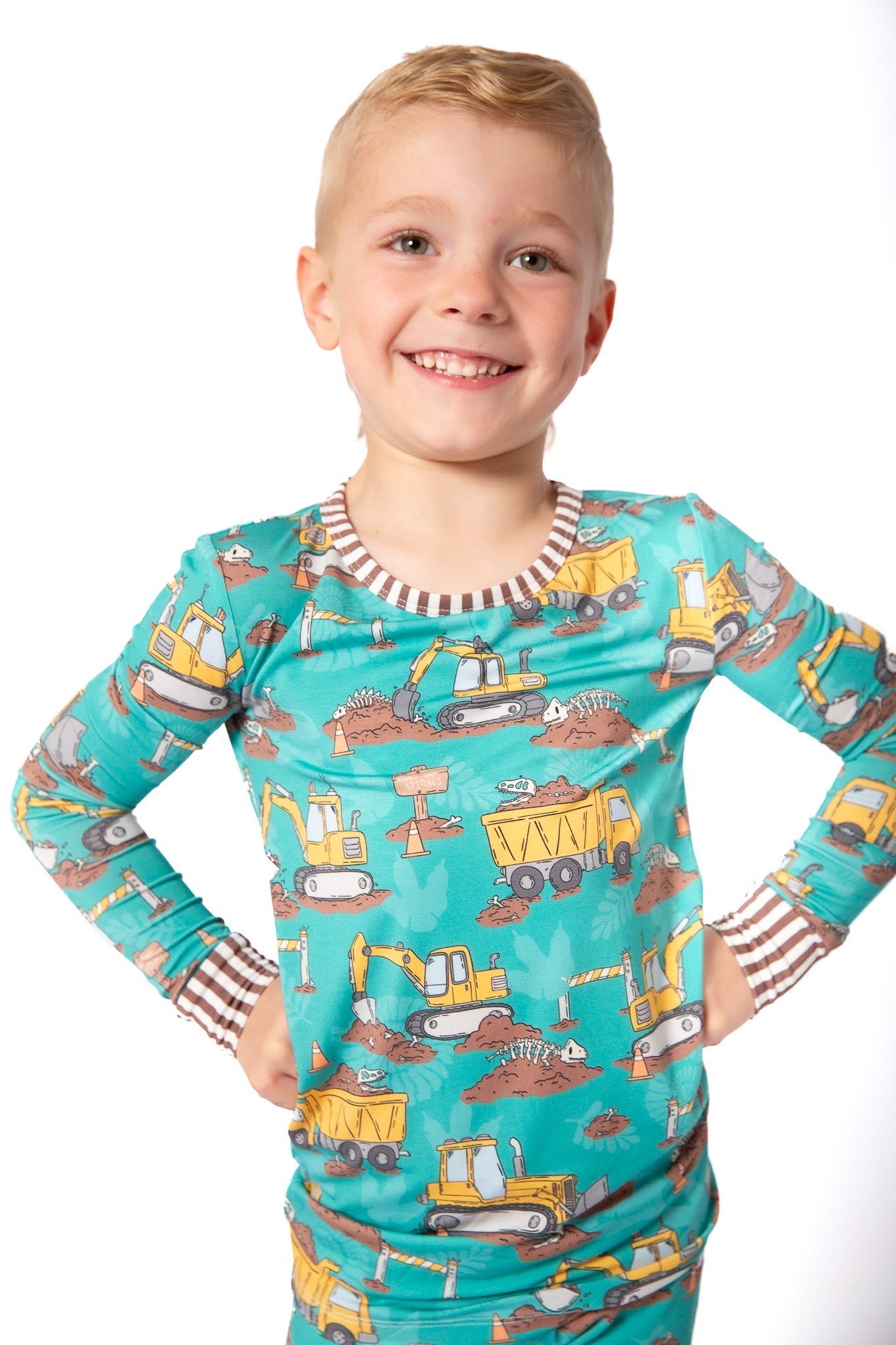 Child wearing a teal long-sleeve shirt with construction vehicle pattern on a white background