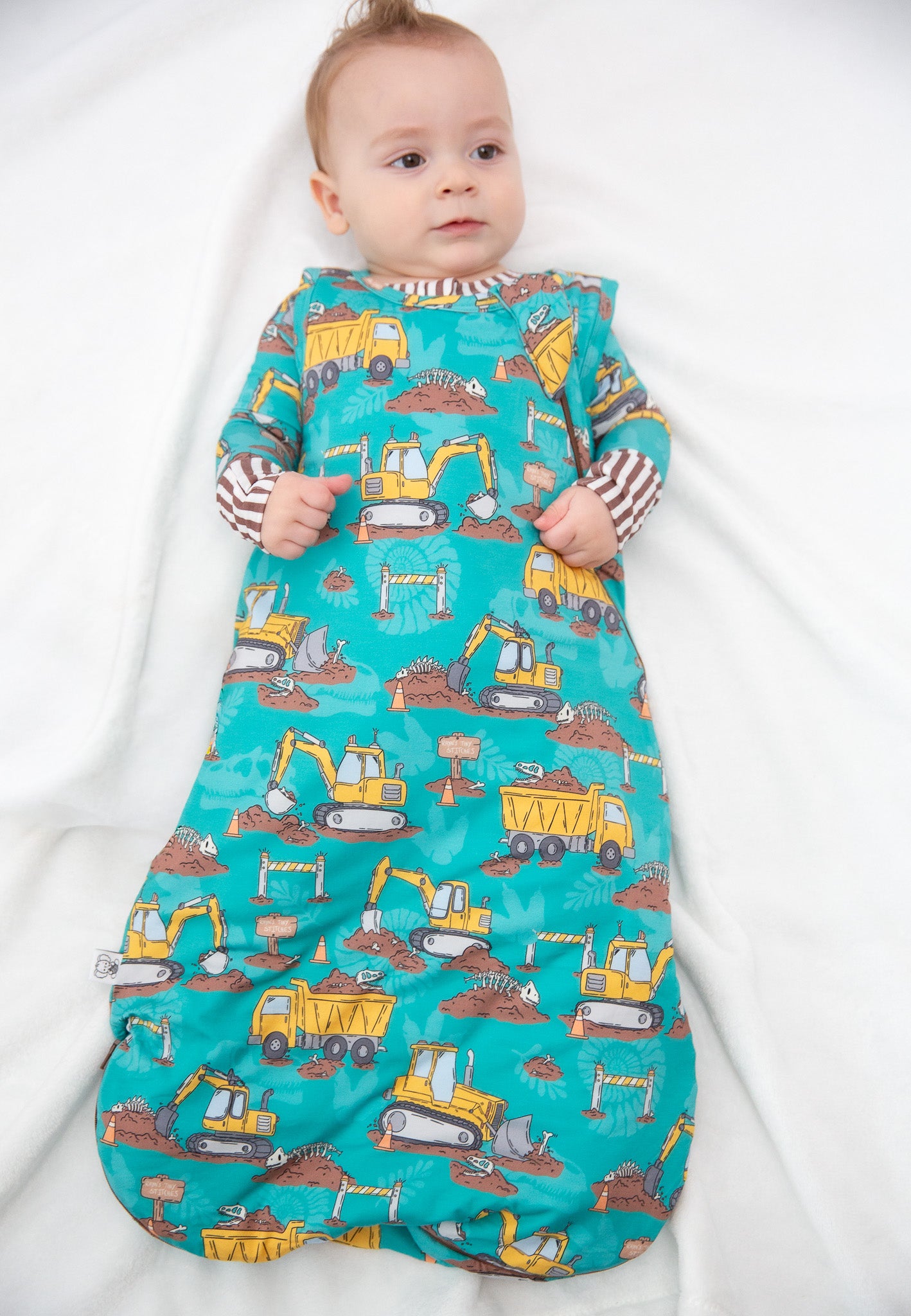 Baby wearing a colorful construction-themed sleep bag on a white background