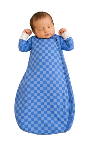 Newborn baby sleeping in a blue checkered swaddle on a beige surface