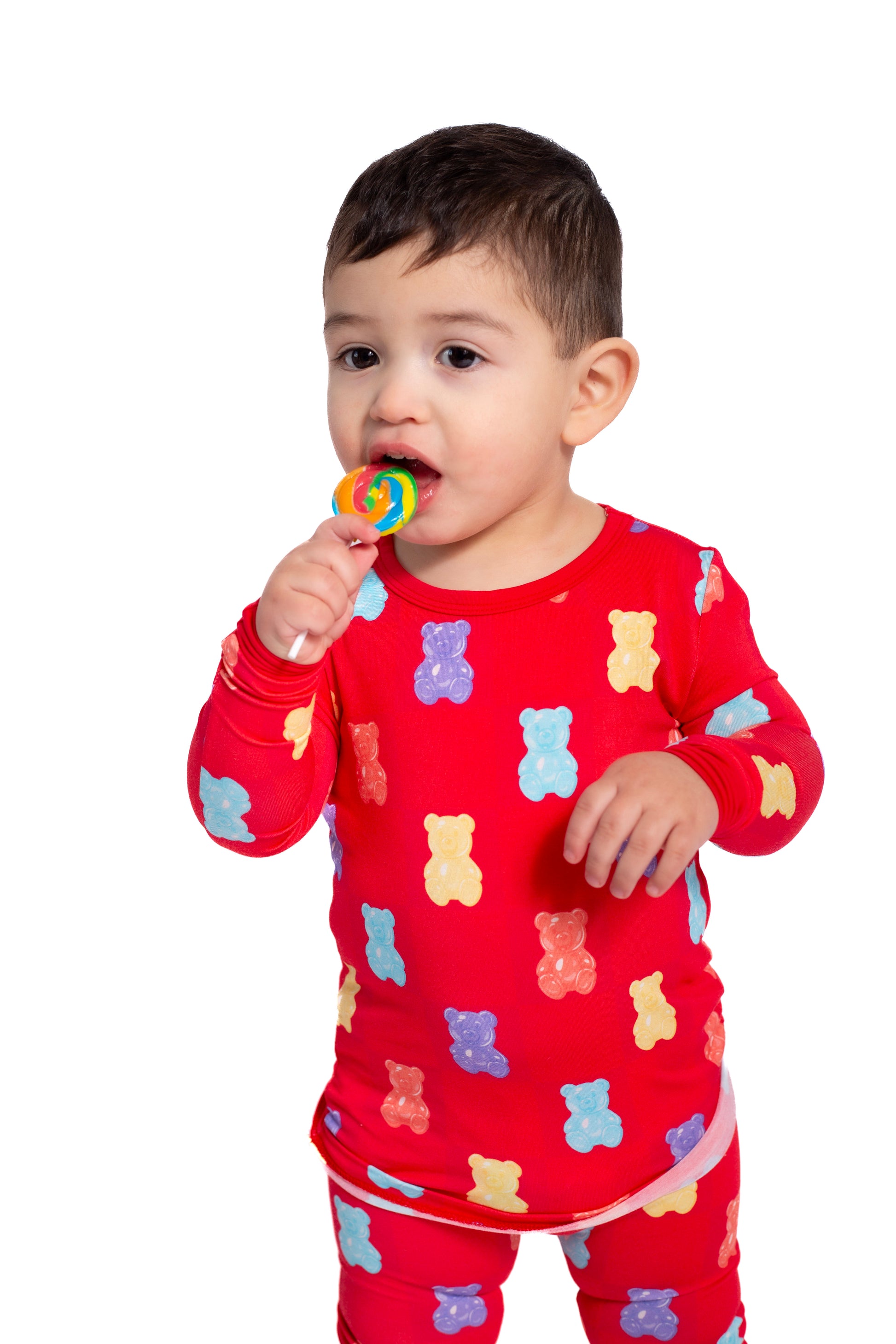 Child wearing a red pajama set with teddy bear patterns, holding a colorful lollipop.