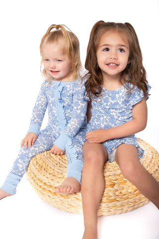 Two children wearing matching blue pajamas with white patterns, sitting on a woven basket.