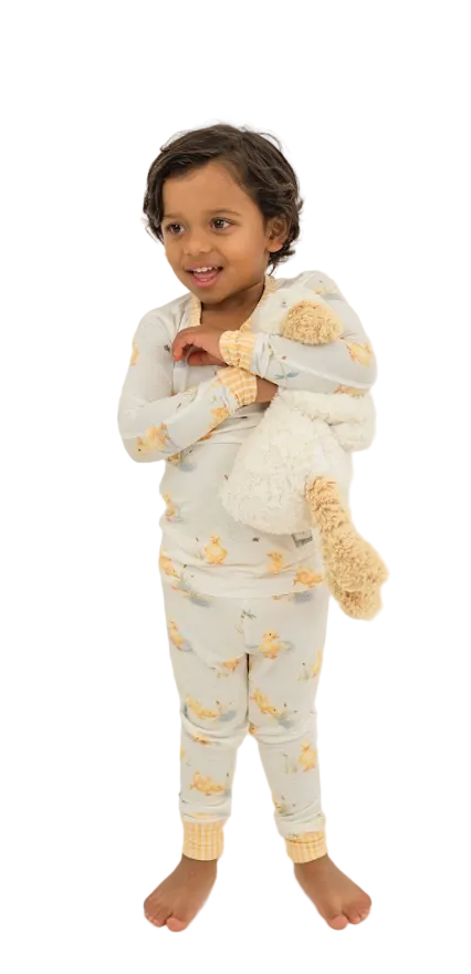 Child wearing a light gray onesie with yellow patterns, holding a plush toy on a white background