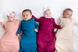 Four babies wrapped in colorful swaddles on a white blanket