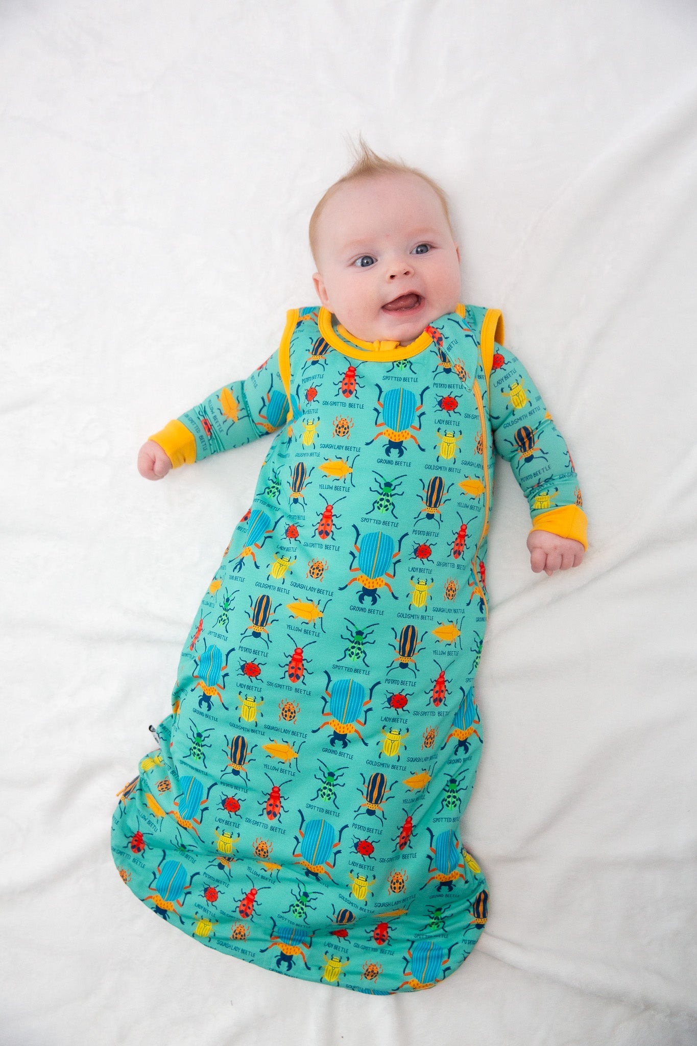 Baby in a colorful dinosaur-patterned onesie lying on a white surface