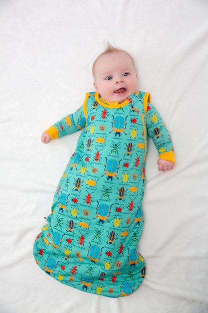 Baby in a colorful dinosaur-patterned onesie lying on a white surface
