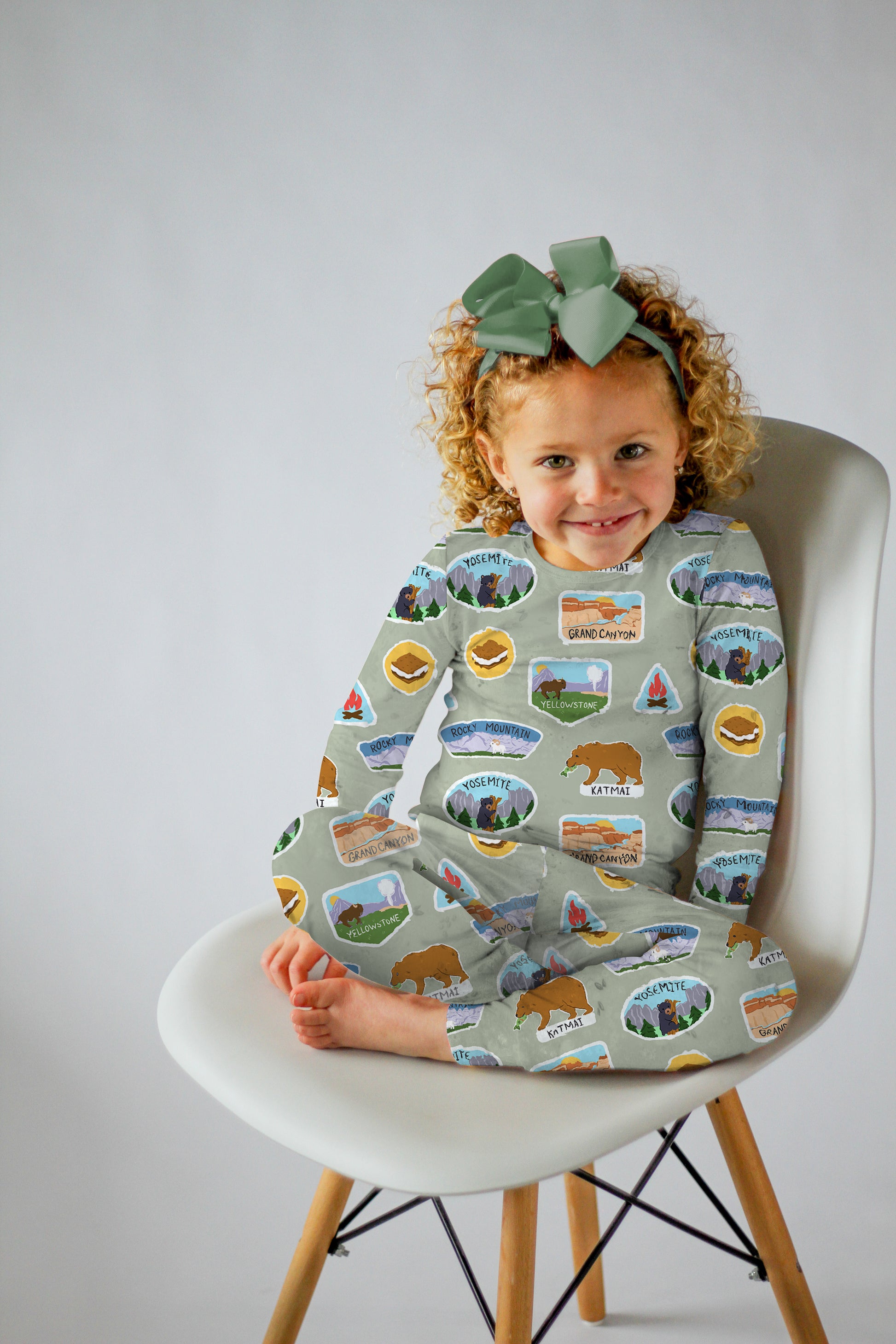 Child wearing a patterned outfit sitting on a chair against a plain background