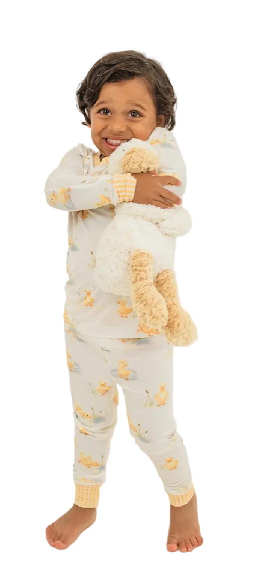 Child wearing a pajama set with a teddy bear design, holding a plush teddy bear on a white background