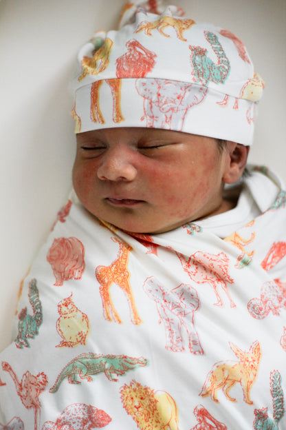 Newborn baby swaddled in a blanket with animal prints, wearing a matching cap.