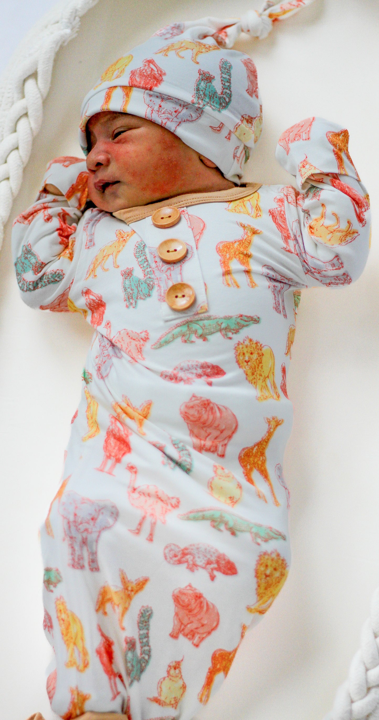 Newborn baby in a patterned outfit and hat lying on a white surface