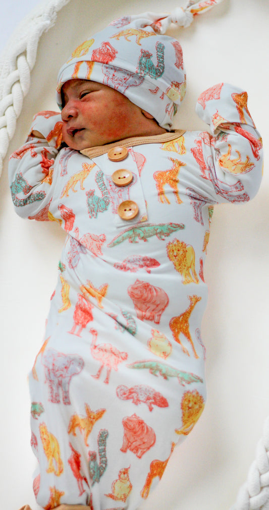 Newborn baby in a patterned outfit and hat lying on a white surface