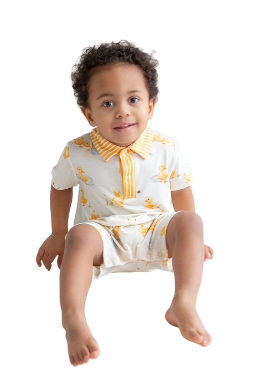 Child wearing a white outfit with yellow patterns sitting on a white floor.