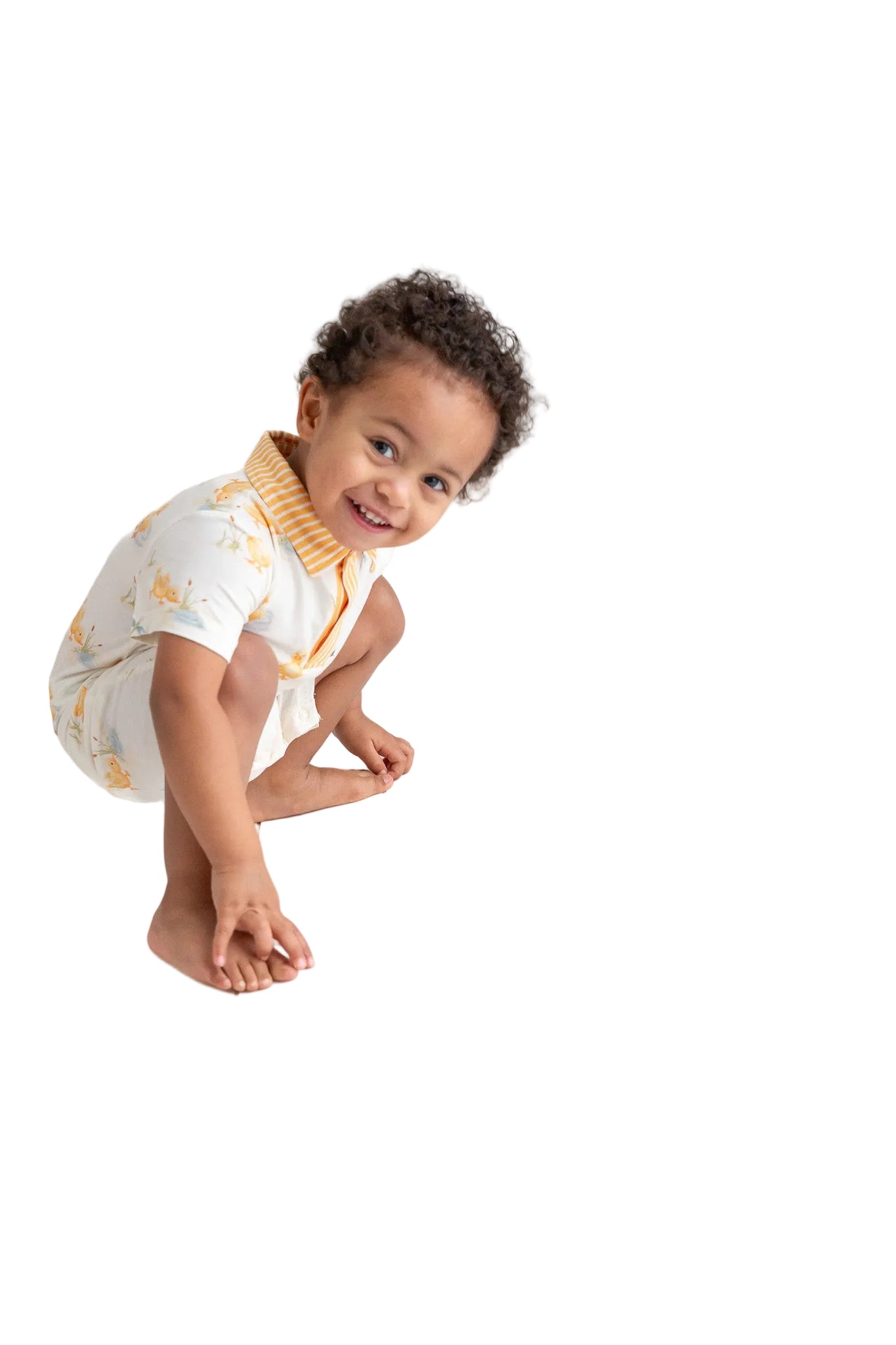 Child wearing a white onesie with yellow patterns on a white floor.