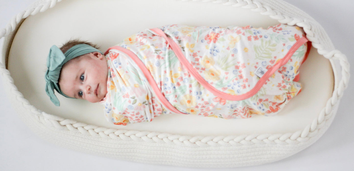 Baby wrapped in a floral swaddle with a headband, lying in a white crib.