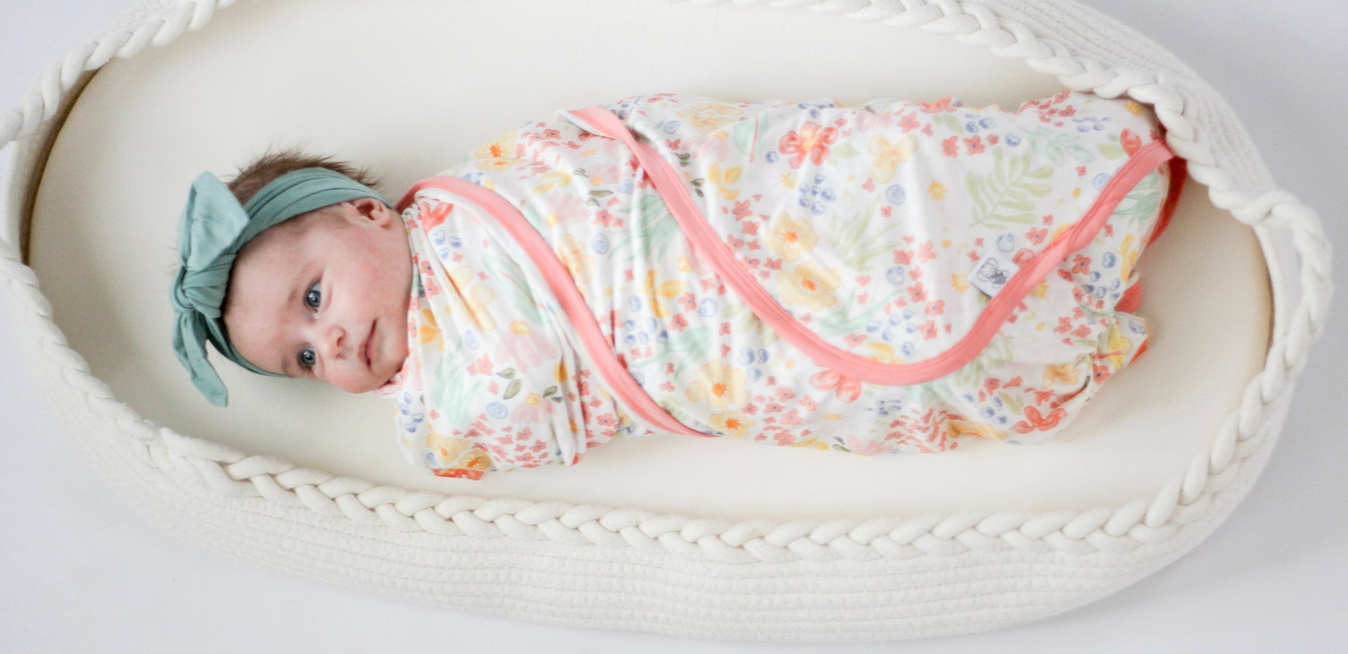Baby wrapped in a floral swaddle with a headband, lying in a white crib.
