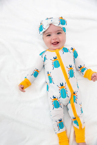 Baby wearing a colorful beetle-patterned onesie with yellow accents on a white background