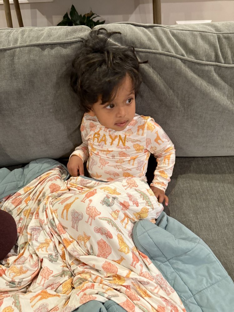 Child sitting on a couch wearing a patterned outfit with 'RAYN' printed on it.
