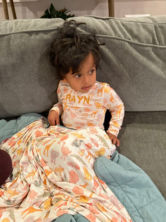 Child sitting on a couch wearing a patterned outfit with 'RAYN' printed on it.