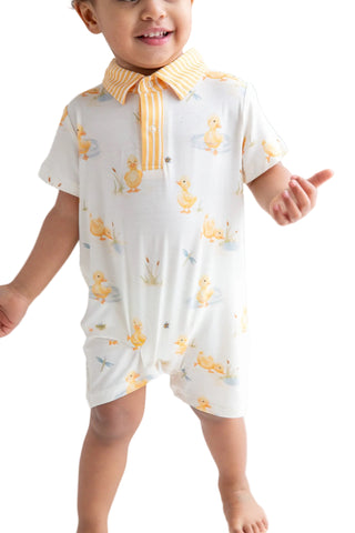 Child wearing a white outfit with yellow duck patterns on a plain background