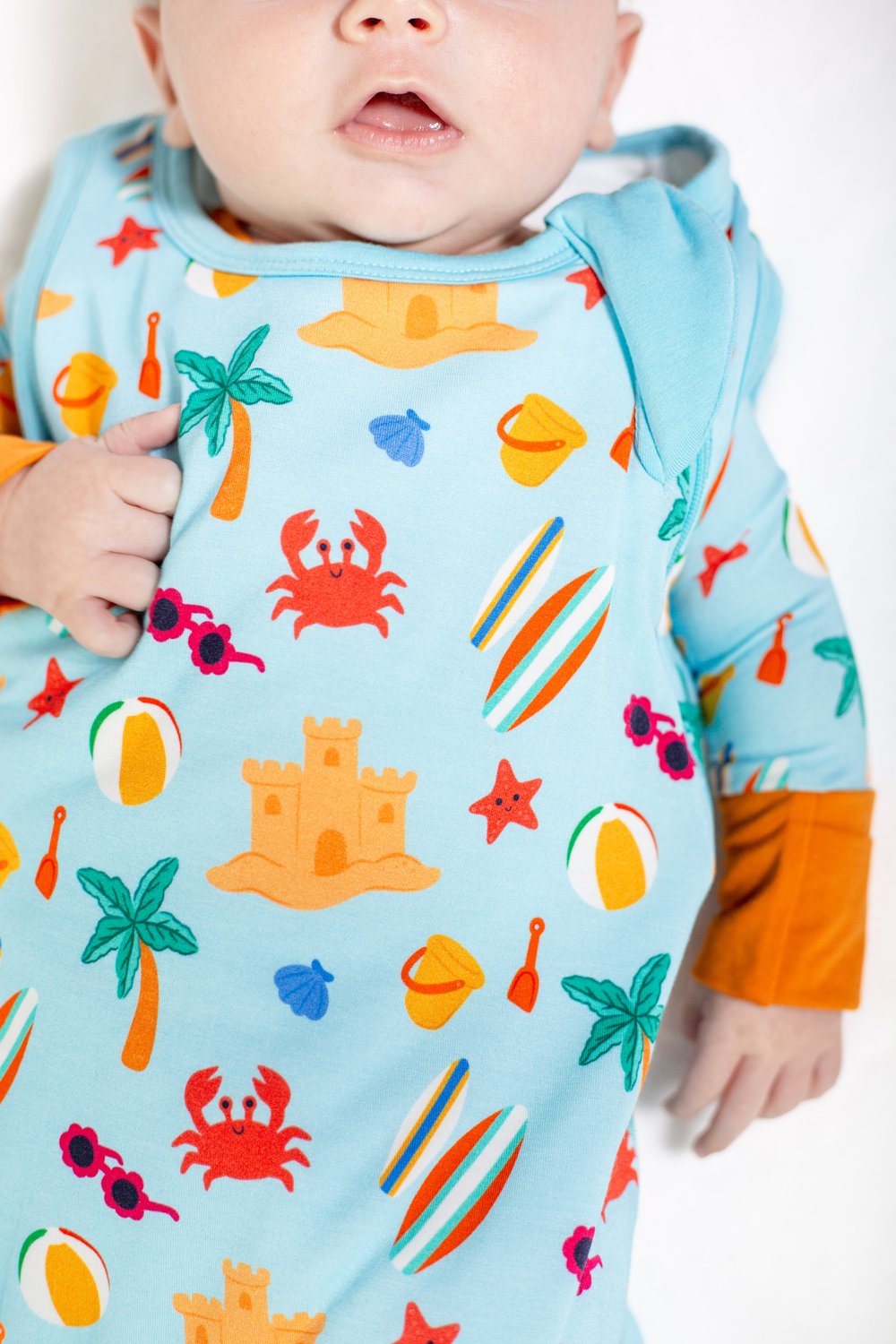 Baby wearing a colorful beach-themed onesie with orange sleeves.