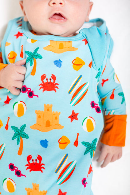 Baby wearing a colorful beach-themed onesie with orange sleeves.