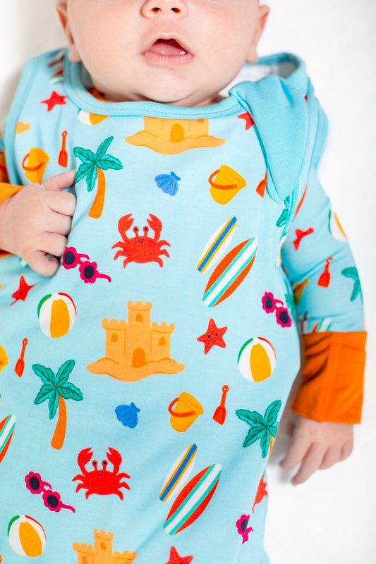 Baby wearing a colorful beach-themed onesie with orange sleeves.