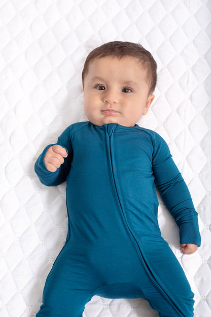 Baby wearing a blue onesie on a white quilted background
