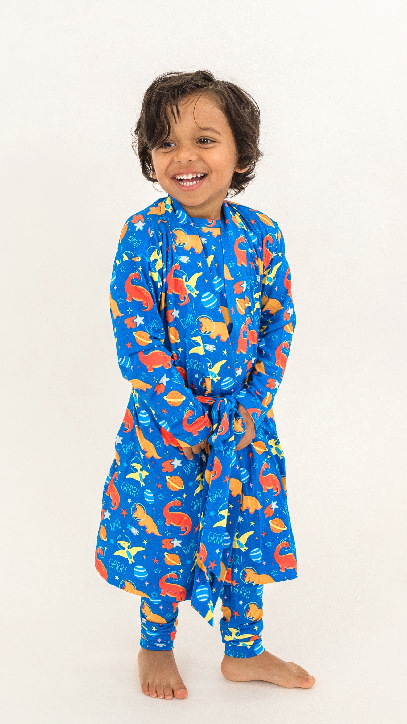 A smiling young child wearing a blue long-sleeve pajama set with a colorful sea creature print, standing against a plain white background.