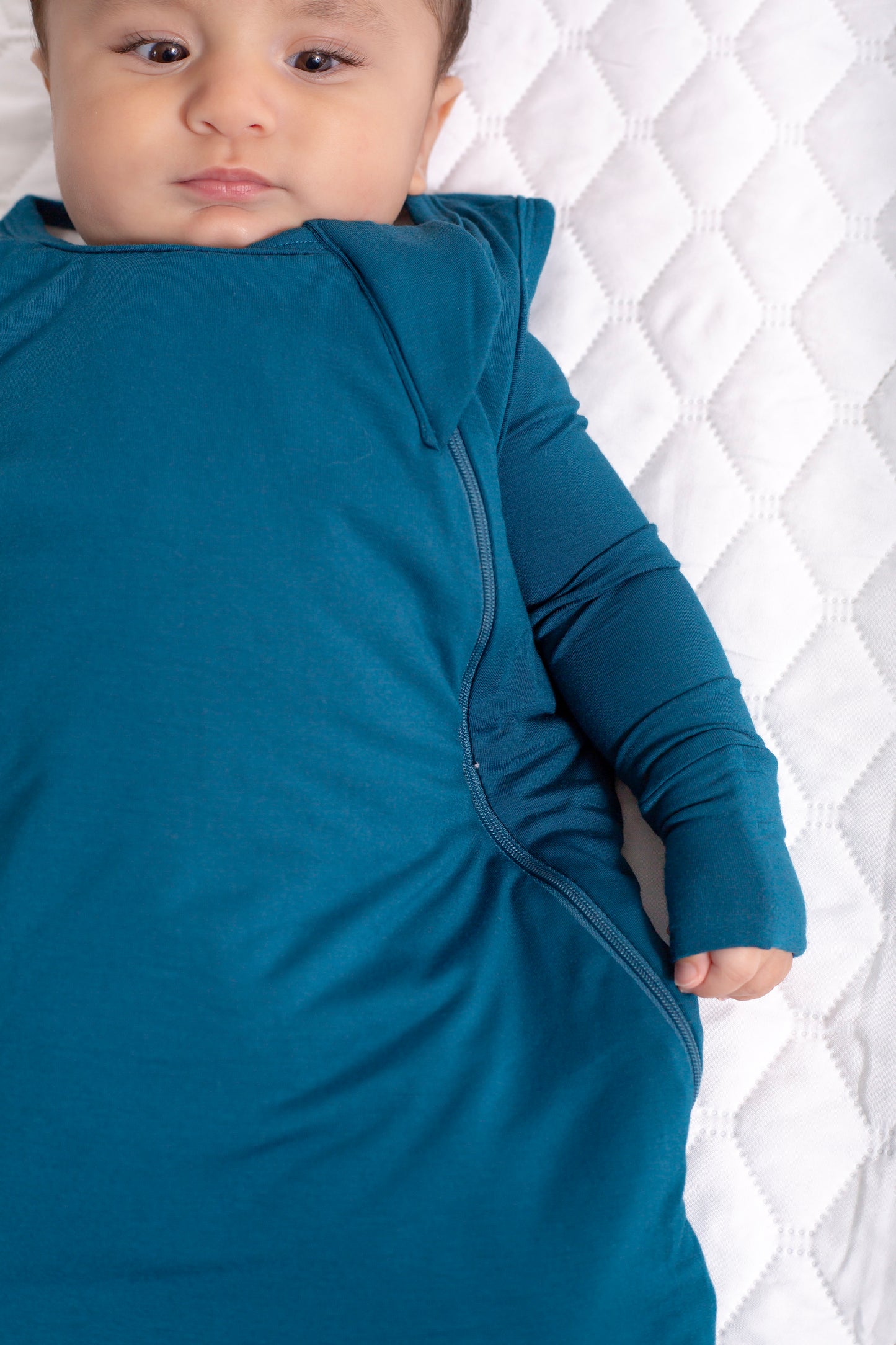 Baby in a blue swaddle against a white quilted background