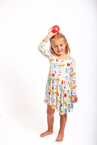 Child wearing a colorful dress with a pattern of cars and food items, holding an apple above their head.