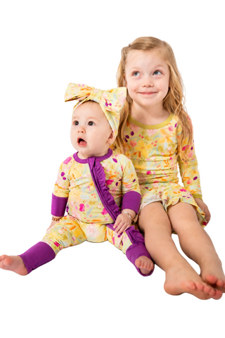 Two children in matching yellow and purple outfits sitting on a white background