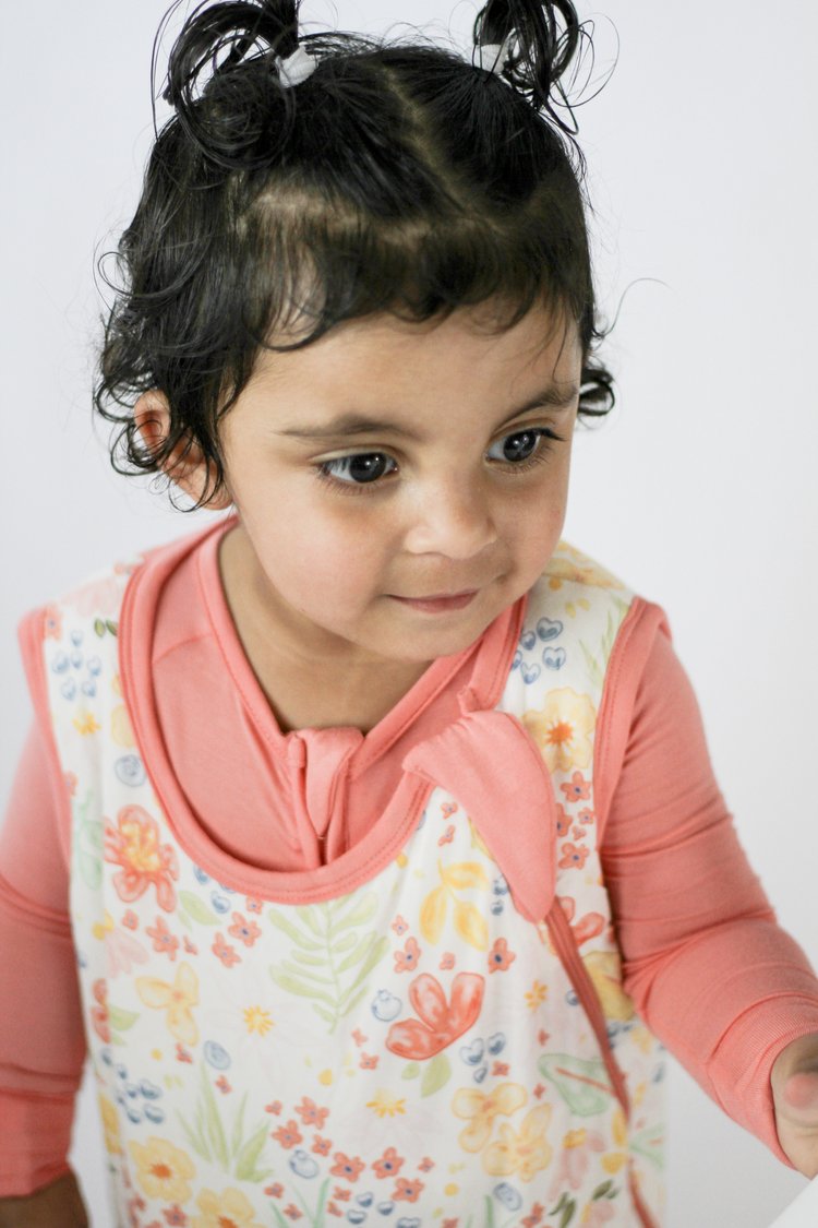 Young girl wearing a floral apron over a pink shirt on a white background