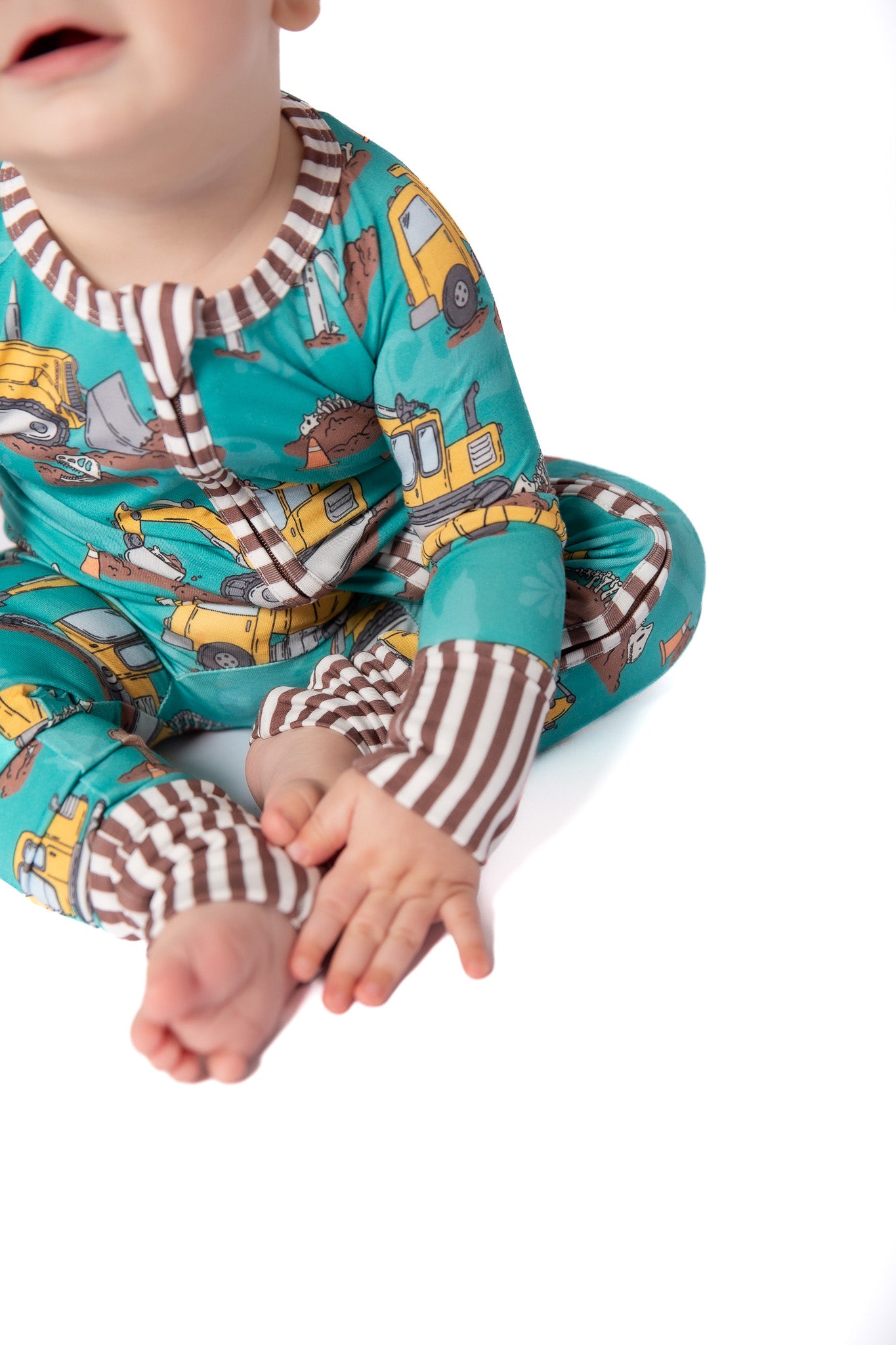 Baby wearing a teal onesie with construction vehicle print on a white background