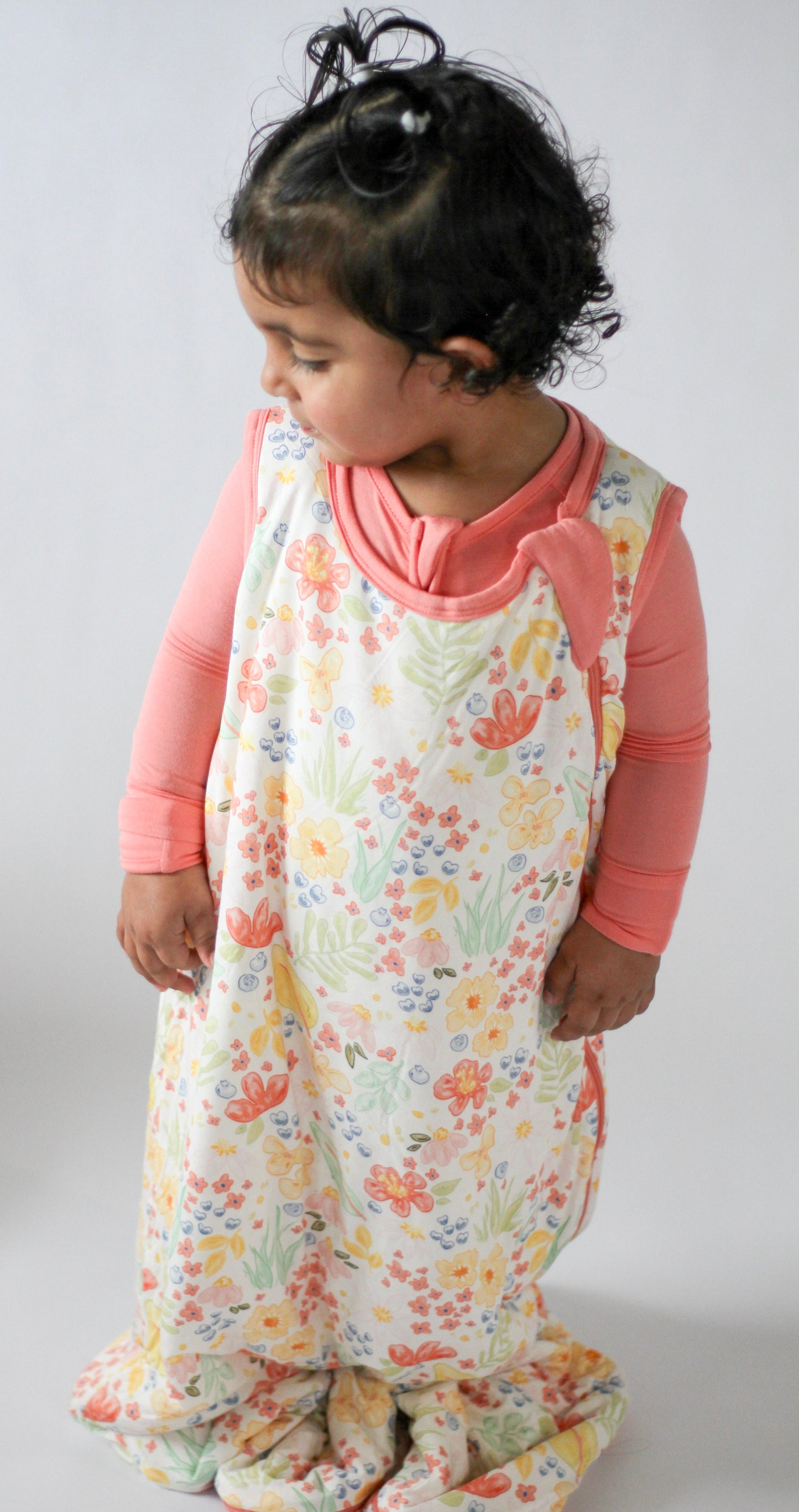 Child wearing a floral onesie with a pink long-sleeve shirt underneath on a plain background