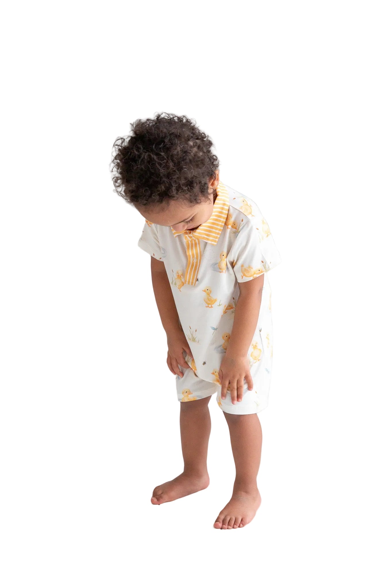 Child wearing a white outfit with yellow patterns on a white floor and background