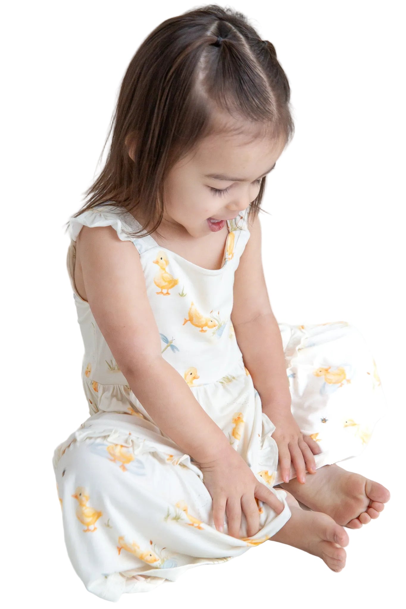 Young child wearing a white dress with yellow duck patterns on a white background