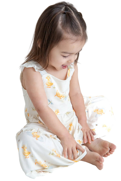 Young child wearing a white dress with yellow duck patterns on a white background