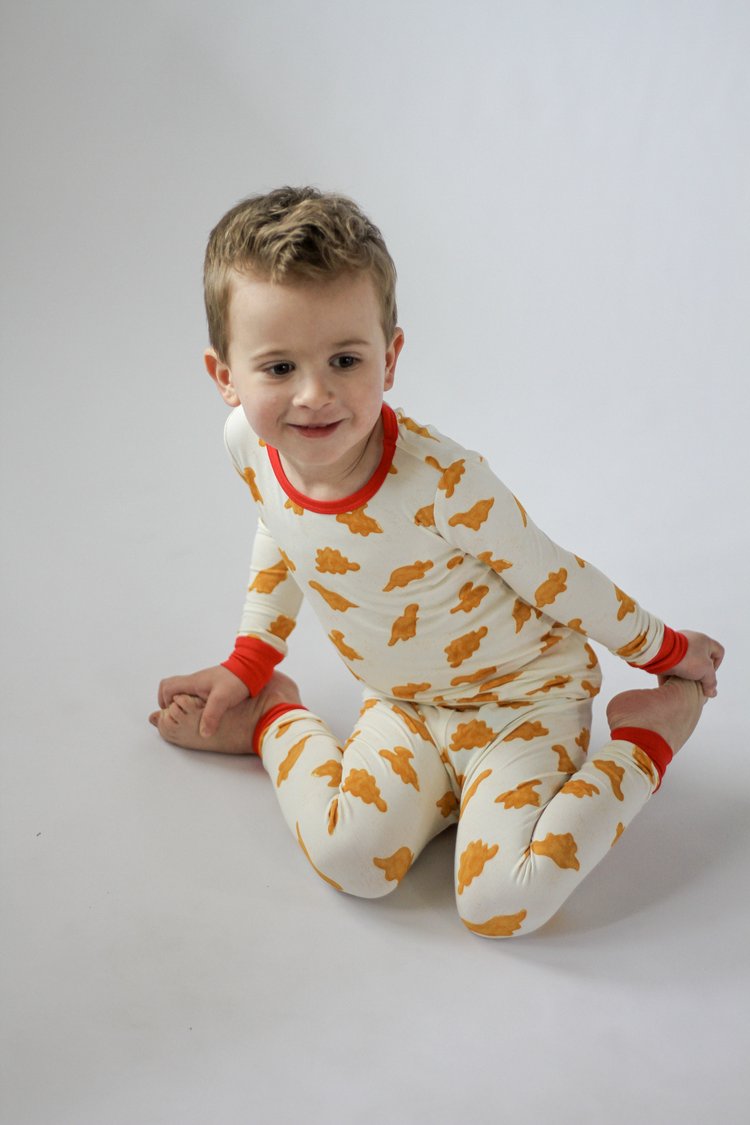 Child wearing a white onesie with orange patterns and red accents on a plain background