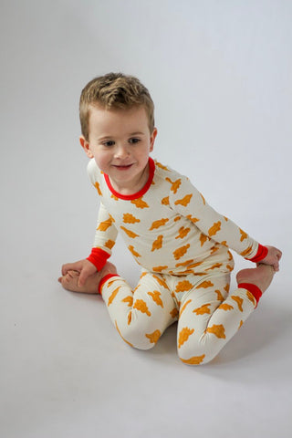 Child wearing a white onesie with orange patterns and red accents on a plain background