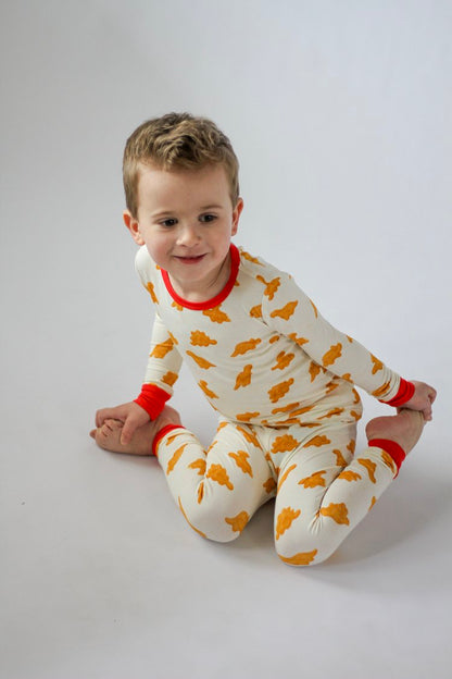 Child wearing a white onesie with orange patterns and red accents on a plain background
