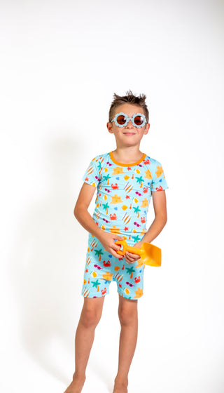 Child wearing a colorful beach-themed outfit with sunglasses on a white background