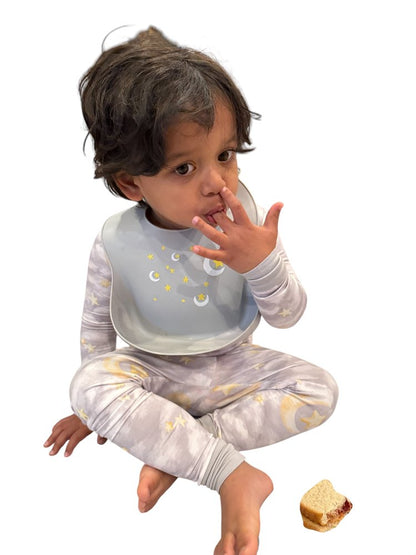 Child wearing a bib and pajamas with a small food item on a white background
