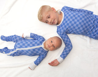 Two children wearing blue checkered onesies lying on a white surface.