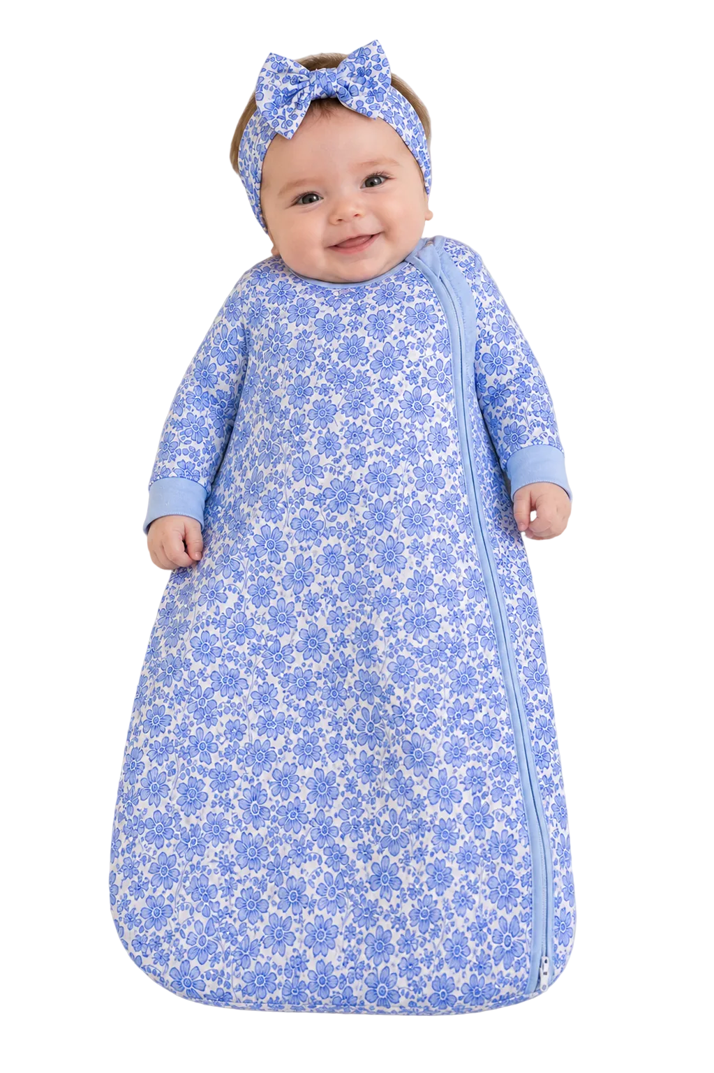 Baby in a blue floral sleeping bag with a matching headband on a beige background