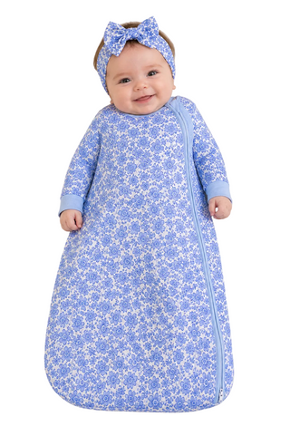 Baby in a blue floral sleeping bag with a matching headband on a beige background