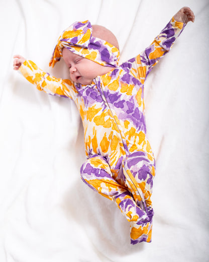 Baby in a purple and yellow patterned outfit on a white background