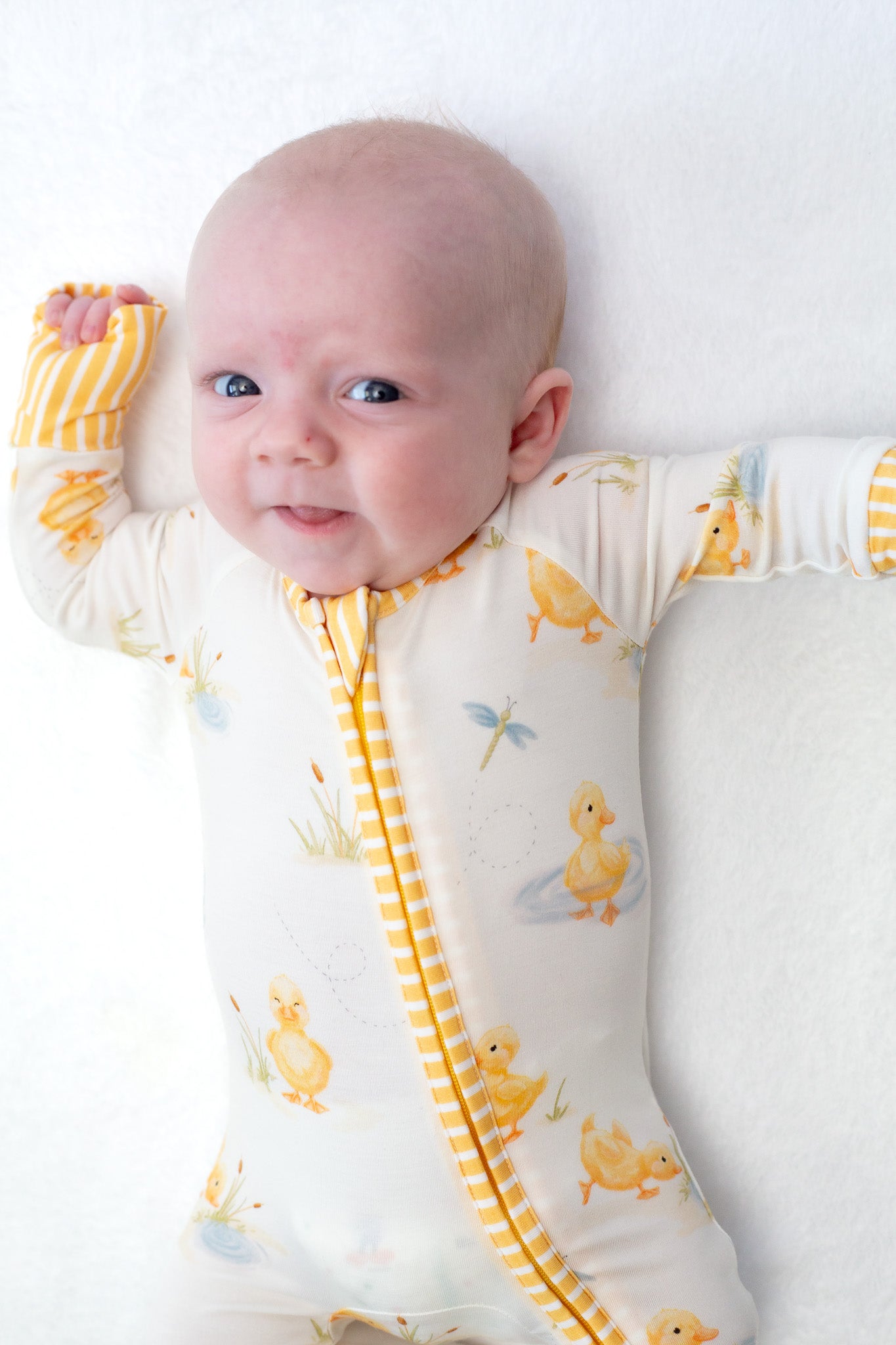 Baby wearing a white onesie with yellow duck patterns on a white background