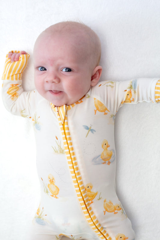 Baby wearing a white onesie with yellow duck patterns on a white background